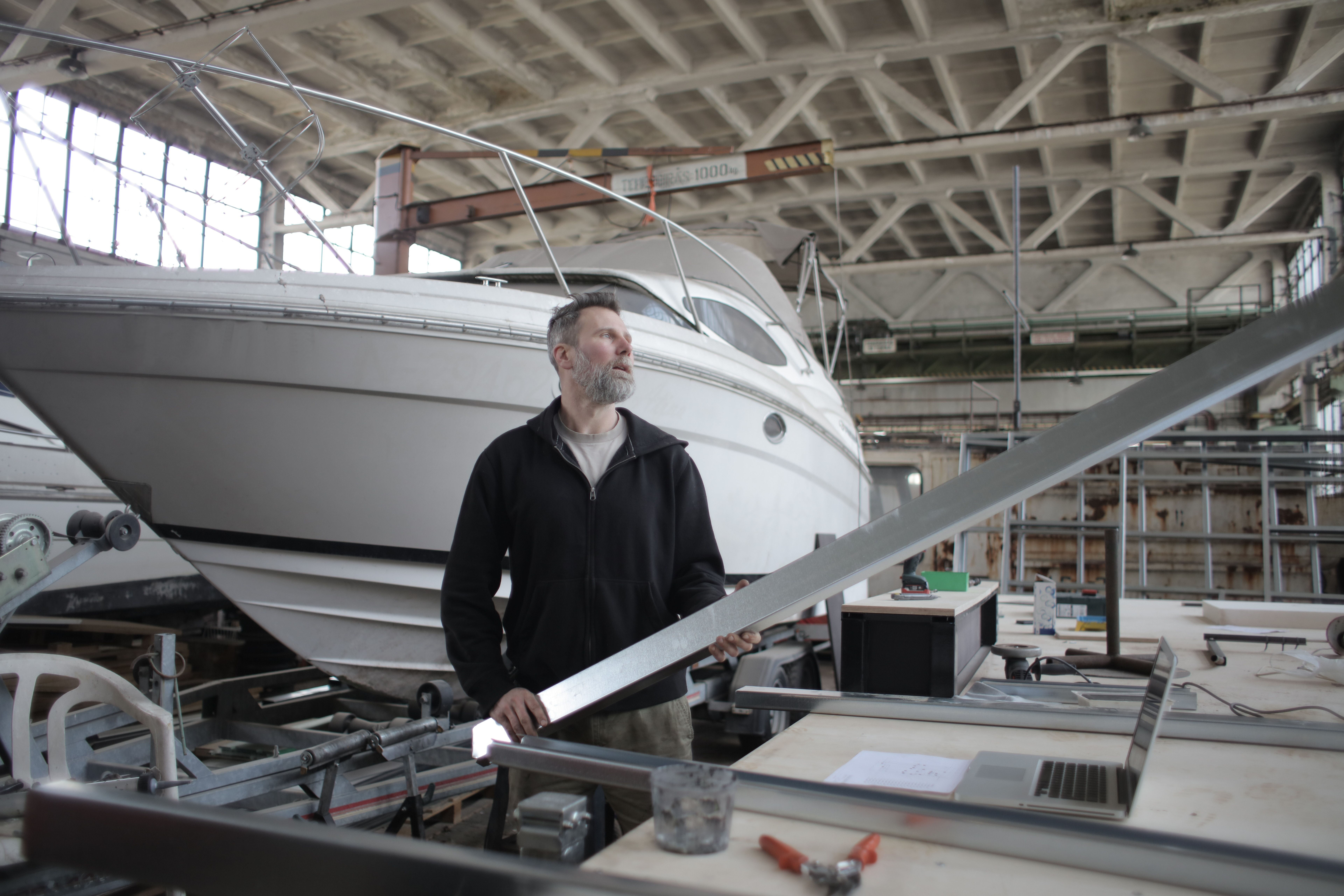Marine technician examining a metal component at a workbench beside a boat.