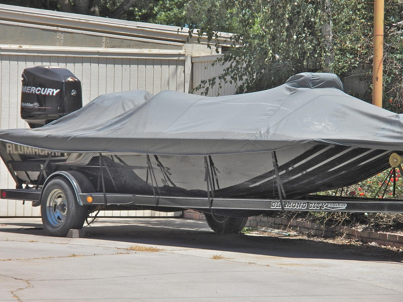 An aluminum fishing boat on a trailer beneath a fitted gray cover, with an outboard motor visible at the stern.